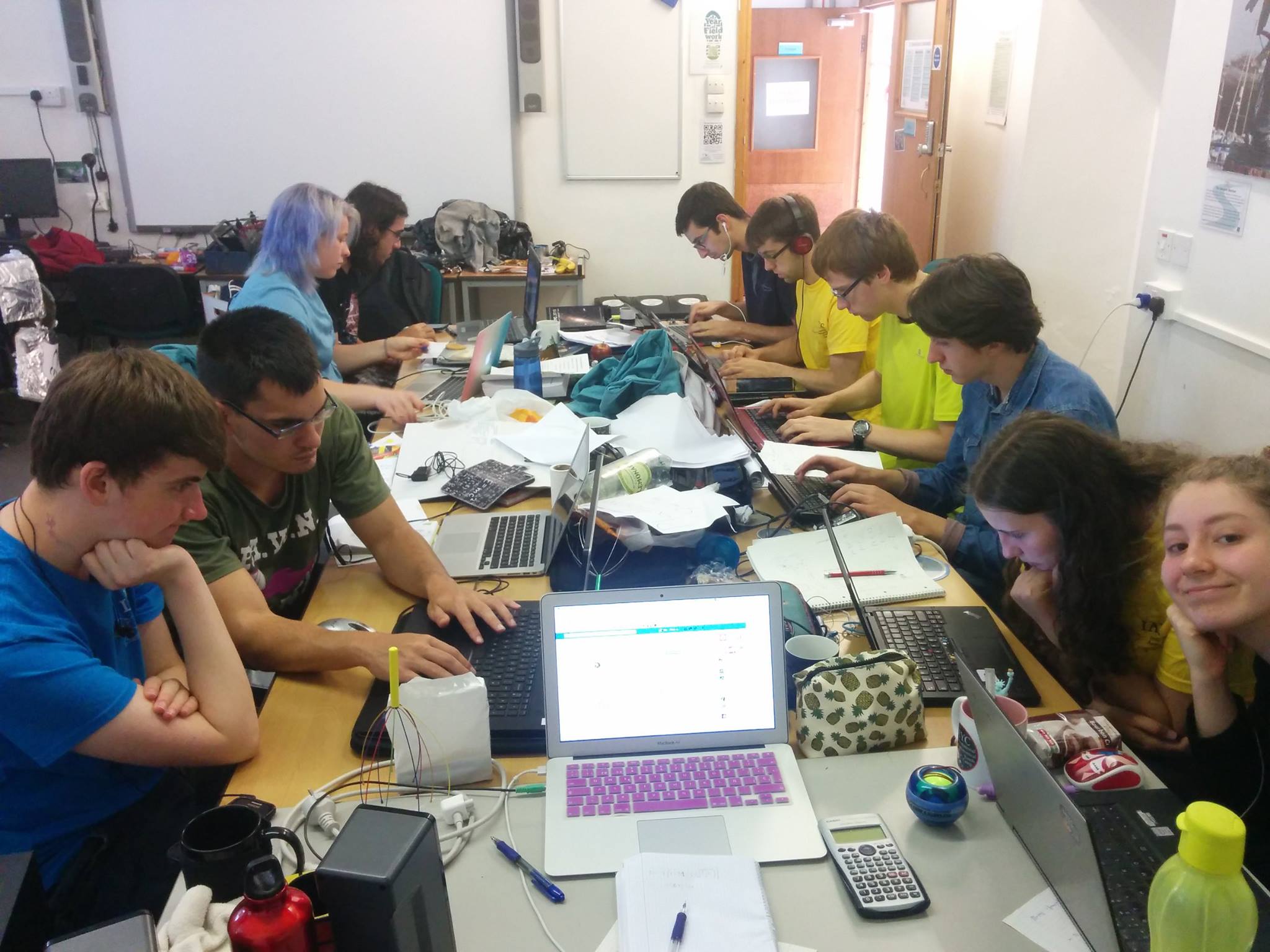 A daytime working group session indoors with participants gathered around a table messy with papers and laptops.