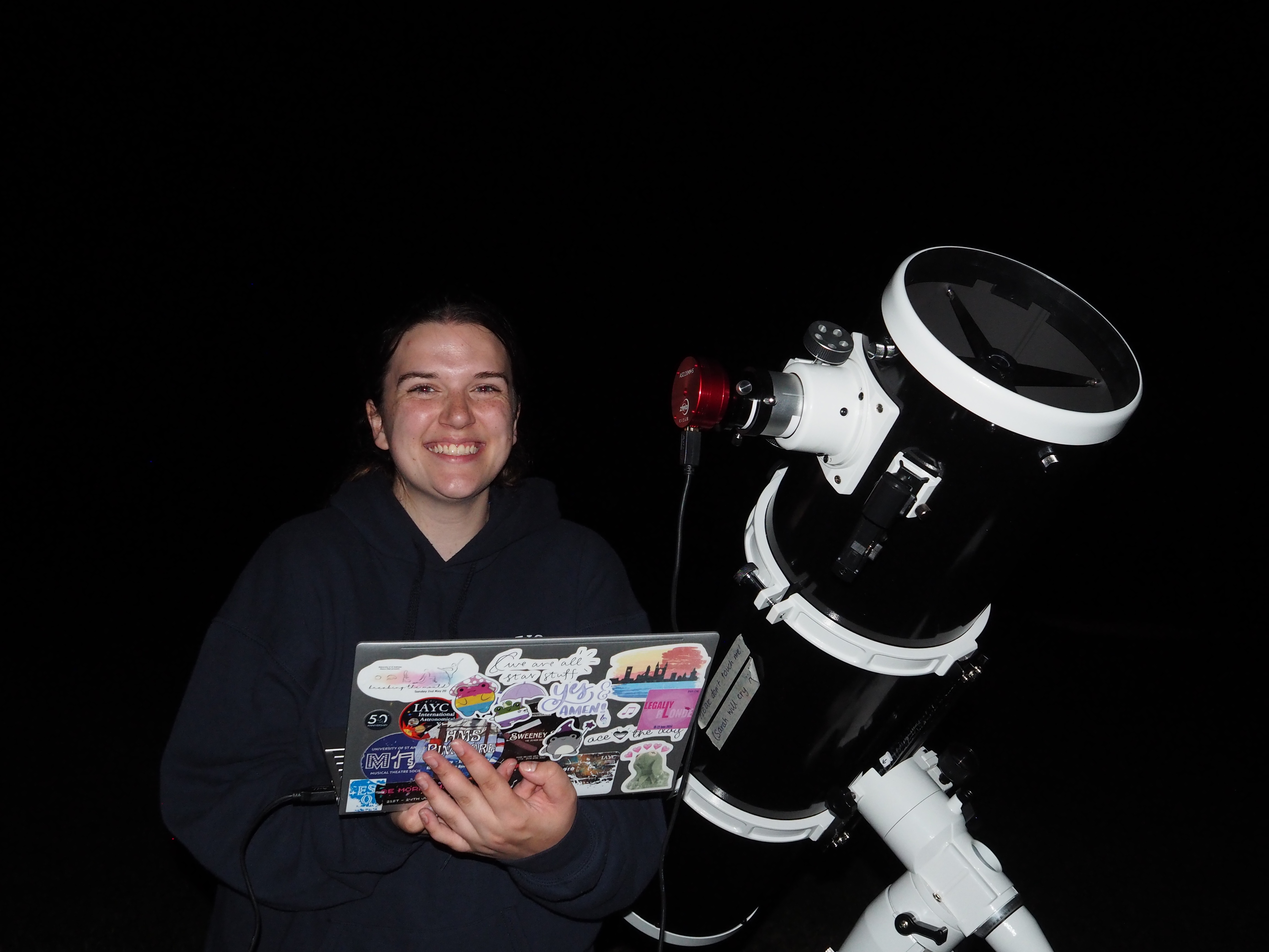 A participant smiling next to a telescope while holding a laptop.